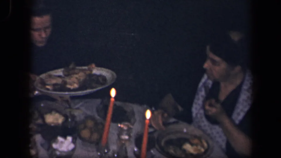 At the 1942 Sebring, Ohio dinner table, a woman holds food near candles while another adult sits beyond a large platter.