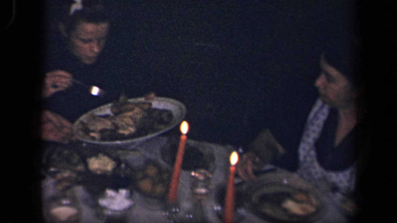 1942 Sebring, Ohio home-movie frame showing adults around a dim candlelit dining table with food platters and glasses.