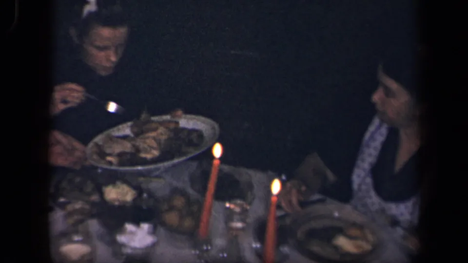 1942 Sebring, Ohio home-movie frame showing adults around a dim candlelit dining table with food platters and glasses.