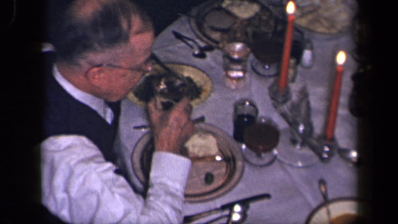 A man in a white shirt and dark vest eats during a candlelit family dinner in the supplied 1942 Sebring, Ohio home-movie context.