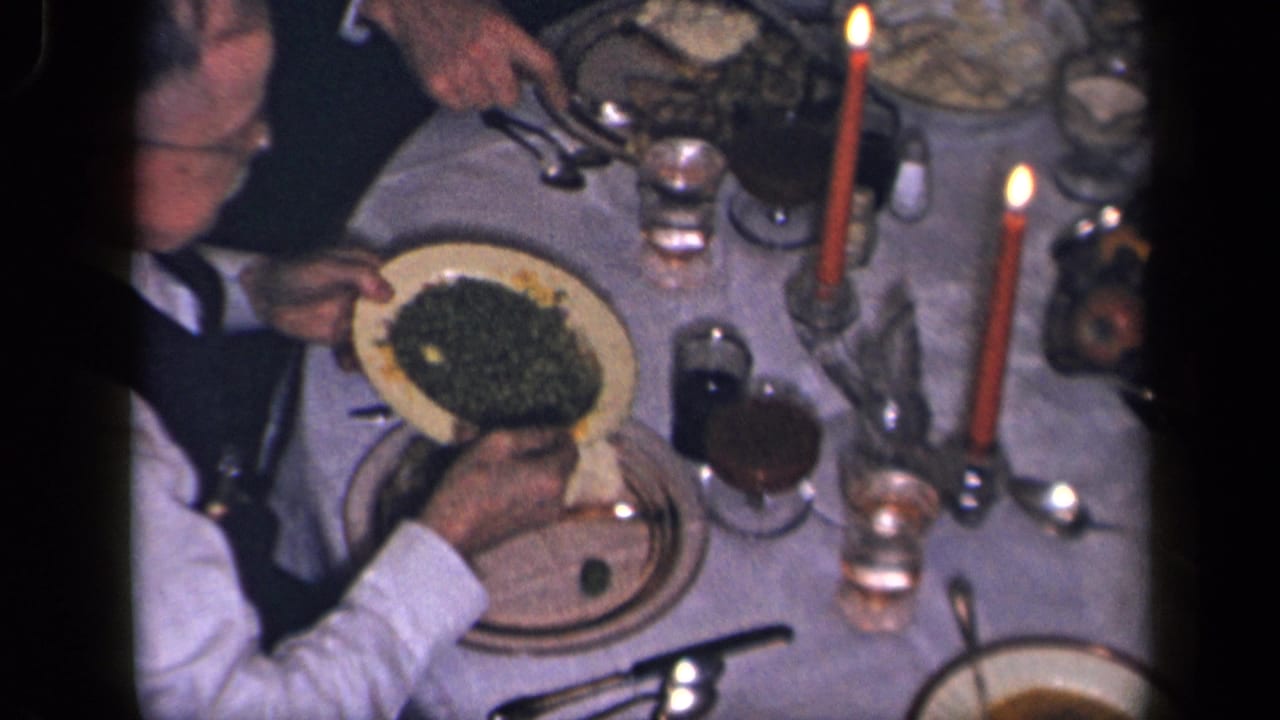 The overhead 1942 Sebring, Ohio frame shows adult hands serving vegetables at a formal table with red candles and glasses.