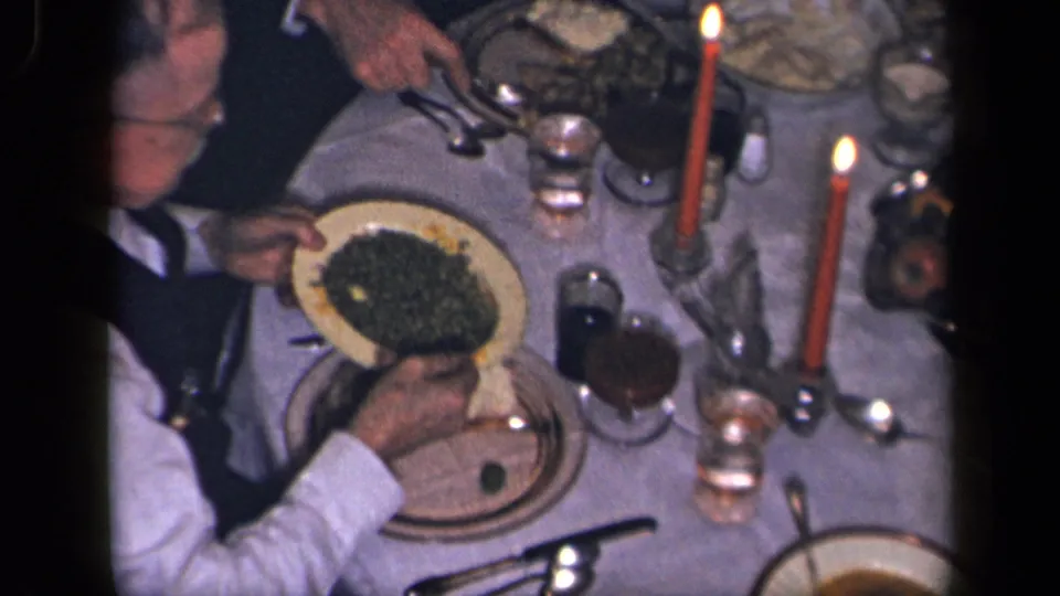 The overhead 1942 Sebring, Ohio frame shows adult hands serving vegetables at a formal table with red candles and glasses.
