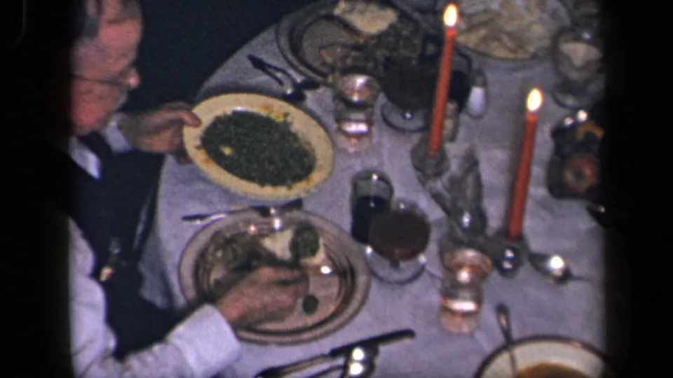 A 1942 Sebring, Ohio home-movie frame shows a seated man and a holiday-style table with candles, dishes, and vegetables.