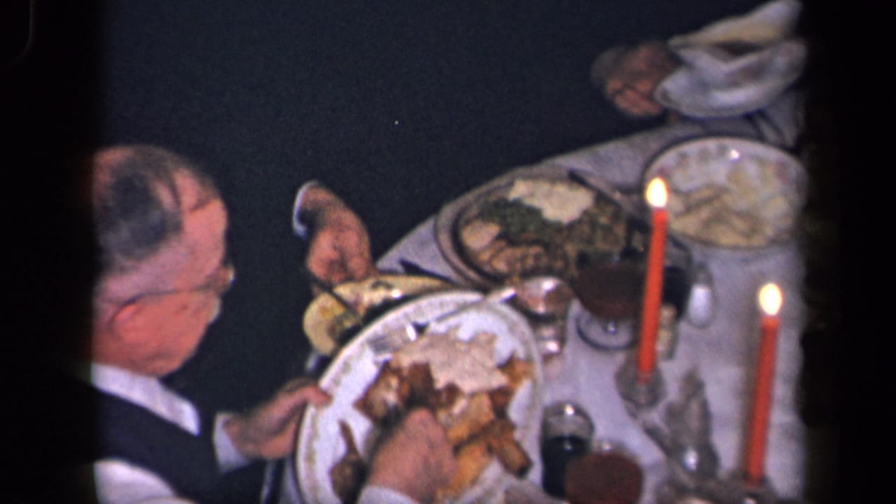 Man at a candlelit dinner table serving food from a plate with roast meat and side dishes.