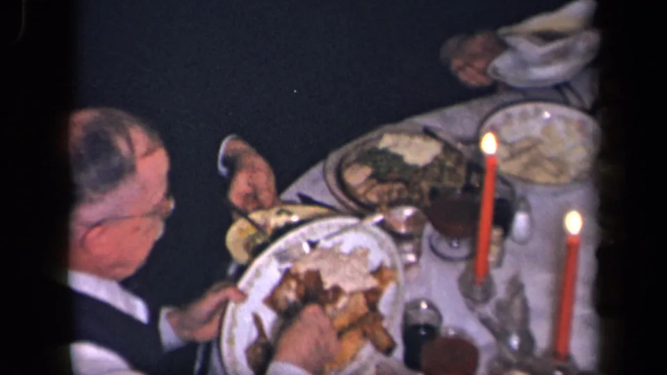 1942 Sebring, Ohio home-movie frame of a suited man serving food at a candlelit family dinner table.