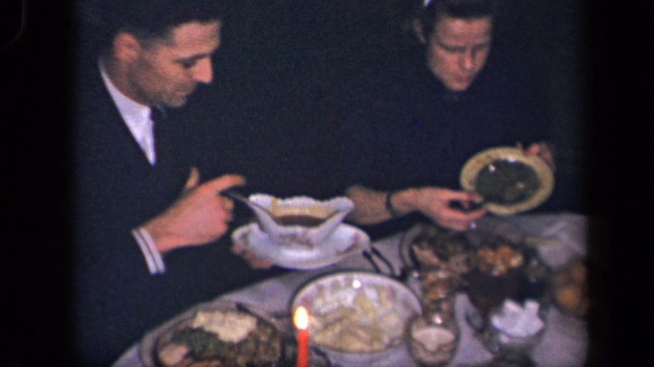 In supported 1942 Sebring, Ohio home-movie footage, two adult men sit at a candlelit dinner table with serving dishes and plates.
