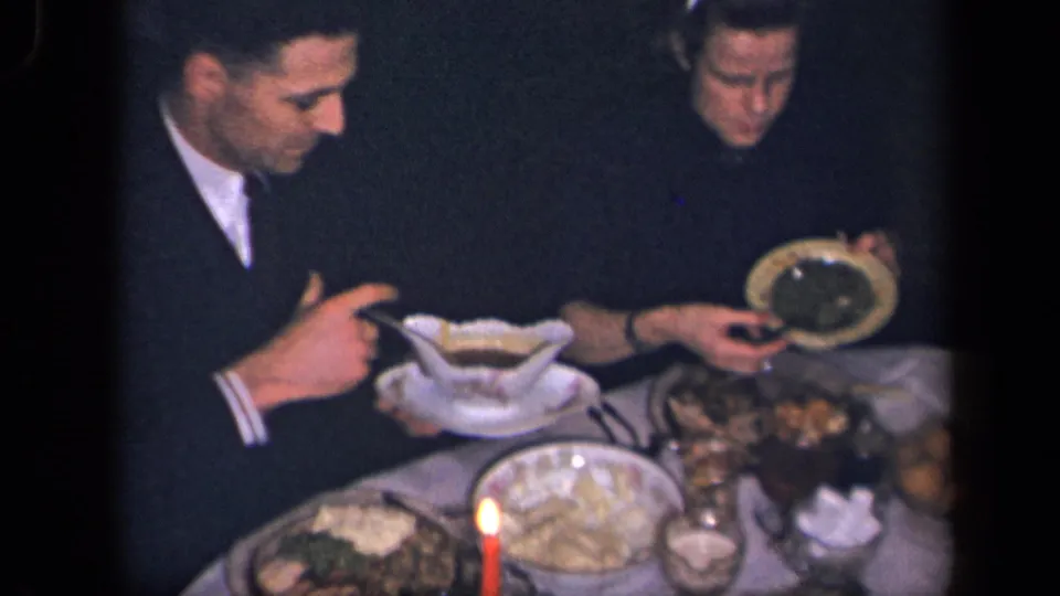 In supported 1942 Sebring, Ohio home-movie footage, two adult men sit at a candlelit dinner table with serving dishes and plates.