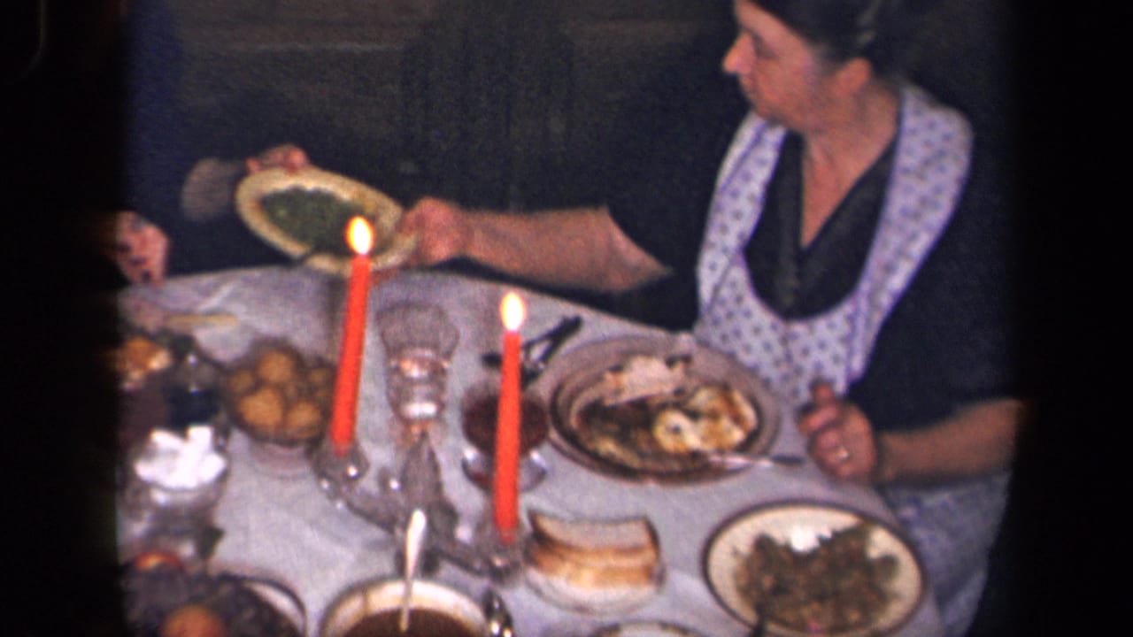 An adult woman in a patterned apron serves food at a candlelit table in supported 1942 Sebring, Ohio home-movie footage.
