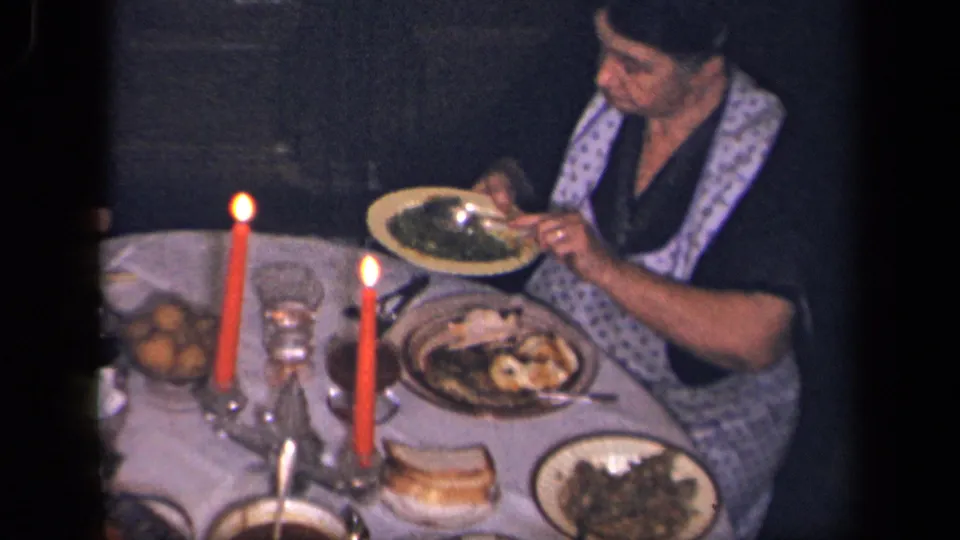 In supported 1942 Sebring, Ohio footage, a woman in an apron eats at a table with red candles, bread, plates, and serving dishes.