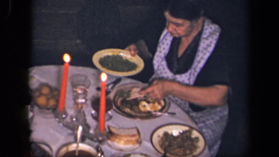 A woman in a patterned apron holds a plate over the candlelit dinner table in supported 1942 Sebring, Ohio home-movie footage.