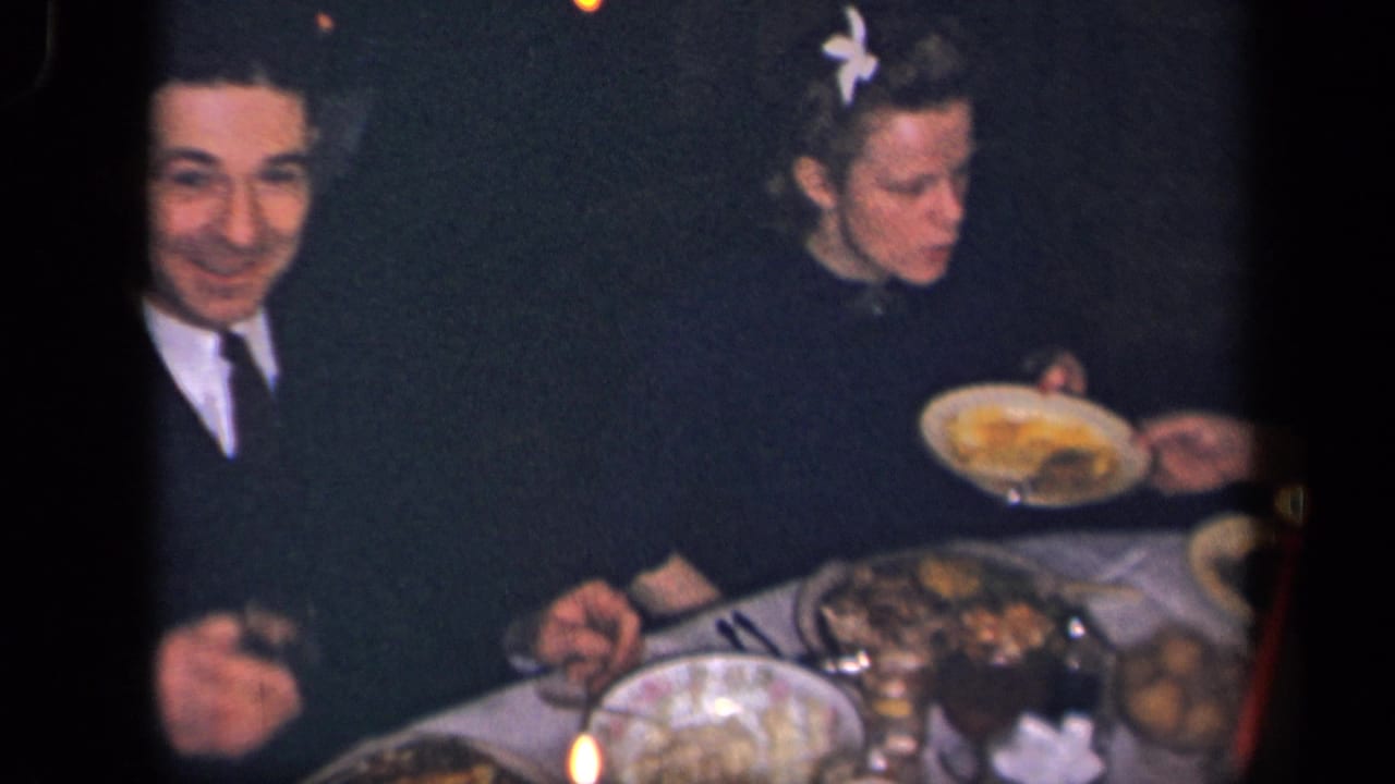 In a 1942 Sebring, Ohio home movie frame, a man in a dark suit and a woman sit at a dim dinner table with food and candles.