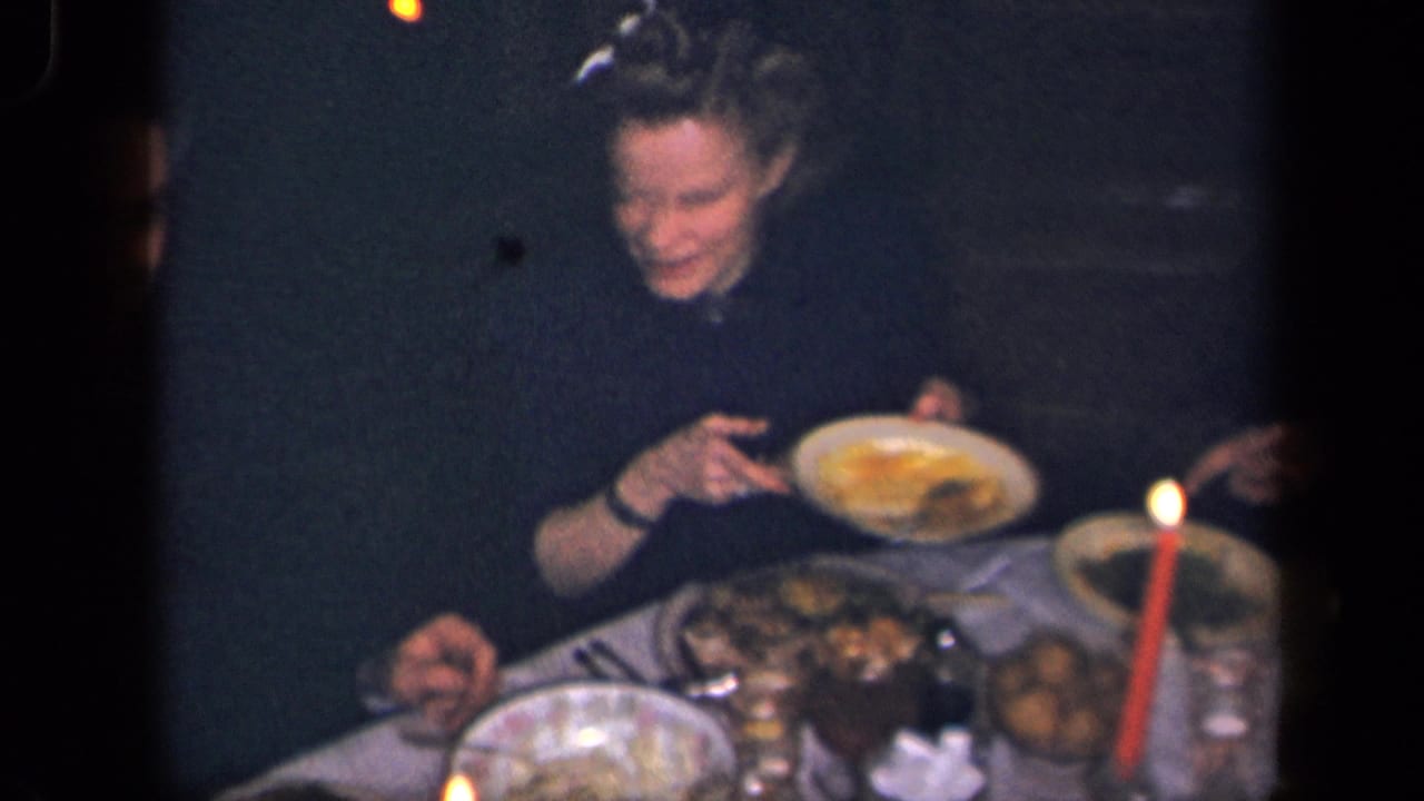 A woman at a 1942 Sebring, Ohio dinner table smiles while holding a plate near serving dishes and a red lit candle.