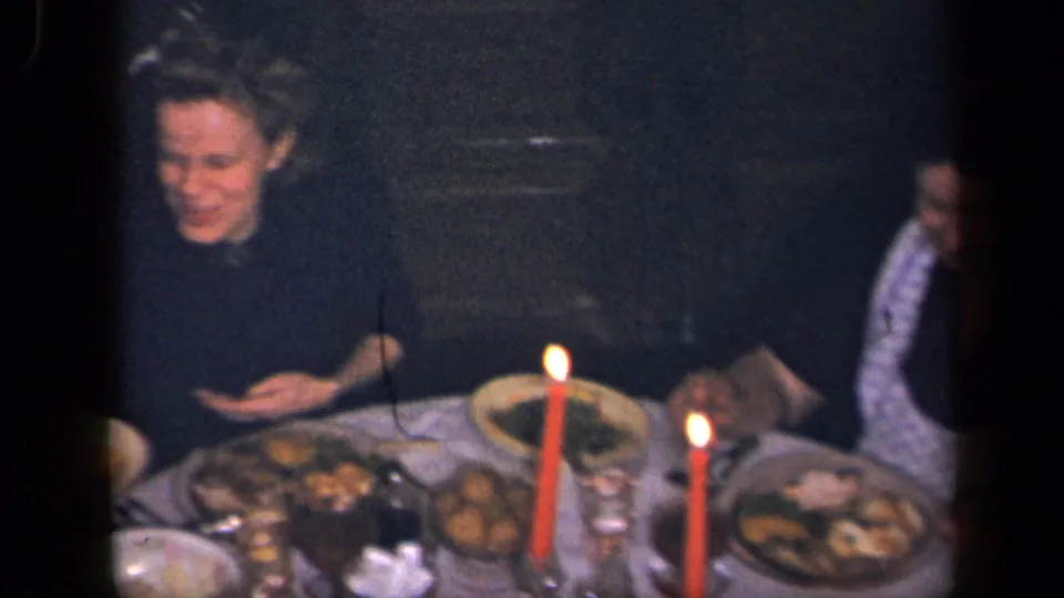 A 1942 Sebring, Ohio home-movie frame shows a woman by a crowded dinner table with red candles and another adult partly visible.