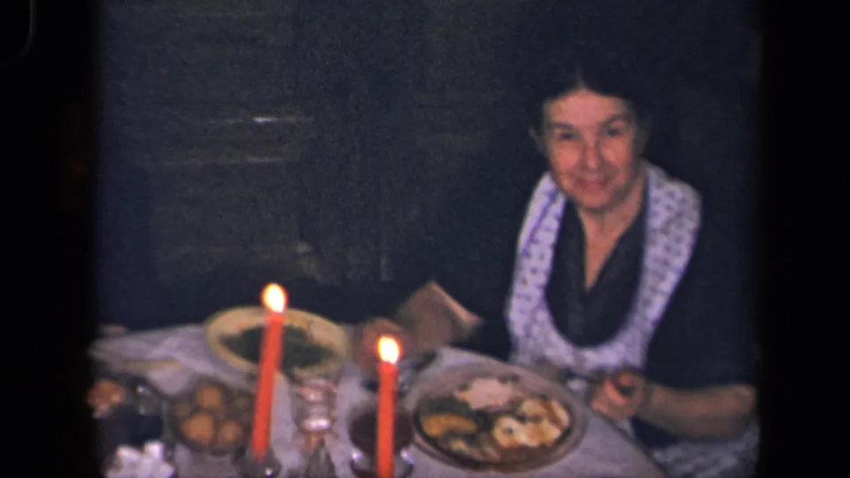 A woman with a light patterned scarf sits beside red candles and shared food in the 1942 Sebring, Ohio home-movie dinner scene.