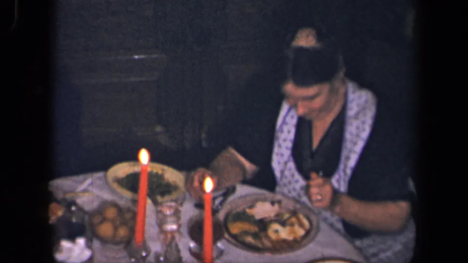 In the stated 1942 Sebring, Ohio home-movie context, a woman in a patterned apron eats at a candlelit table set with food.