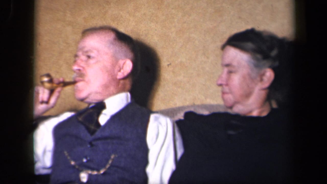 In the Sebring, Ohio home interior, the older man smokes a pipe while the woman watches from beside him.