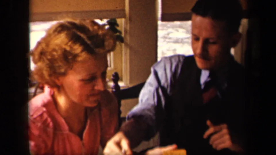 The couple lean toward each other in the warm interior as the man reaches forward and the woman looks down, suggesting shared food or table activity.