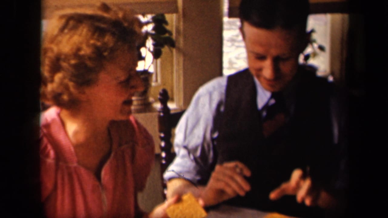 In a 1942 Sebring, Ohio home-movie frame, a woman in a pink blouse smiles as a man in a vest sits beside her at breakfast.