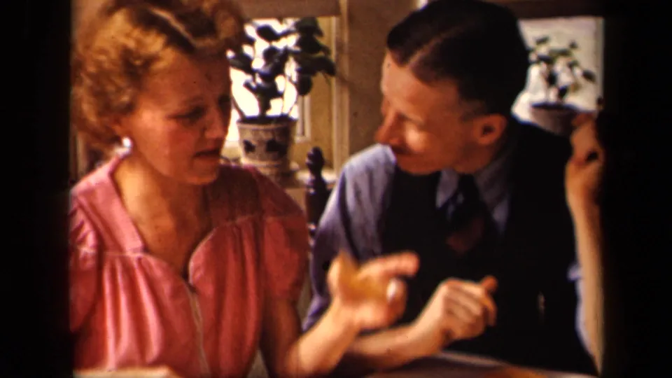 In the 1942 home-movie scene, the woman gestures with one hand while the man turns toward her in close conversation.