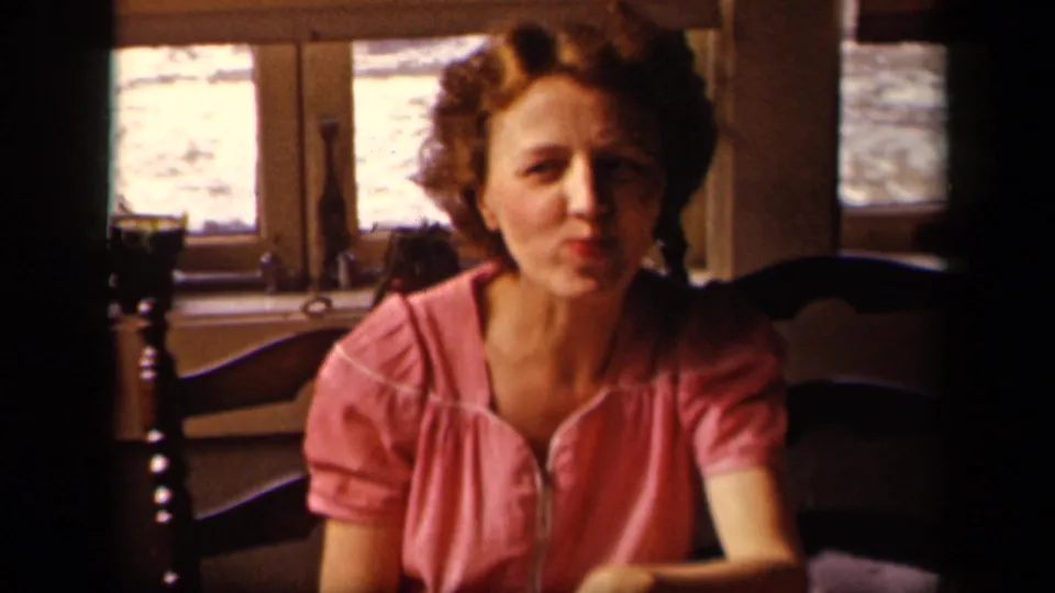 Young woman in a pink blouse sits at a table in a Sebring, Ohio home-movie interior from 1942, facing the camera.