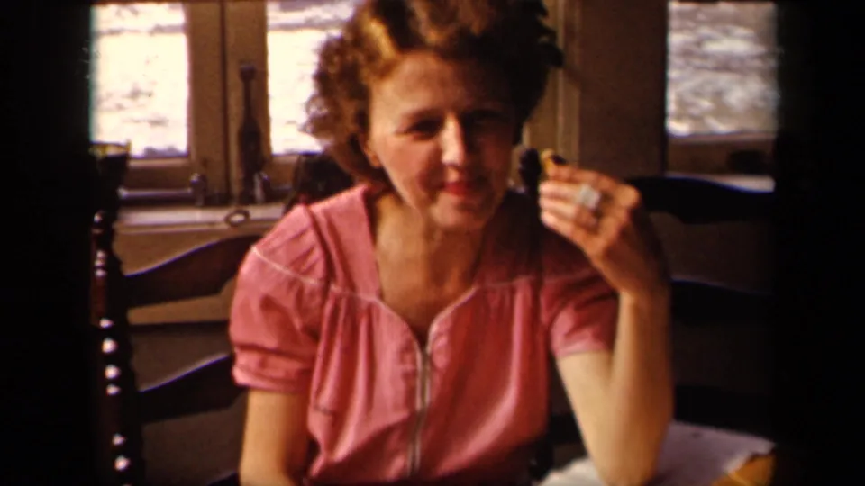 Young woman seated at a table holds a small piece of food near her face in 1942 Sebring, Ohio home-movie footage.