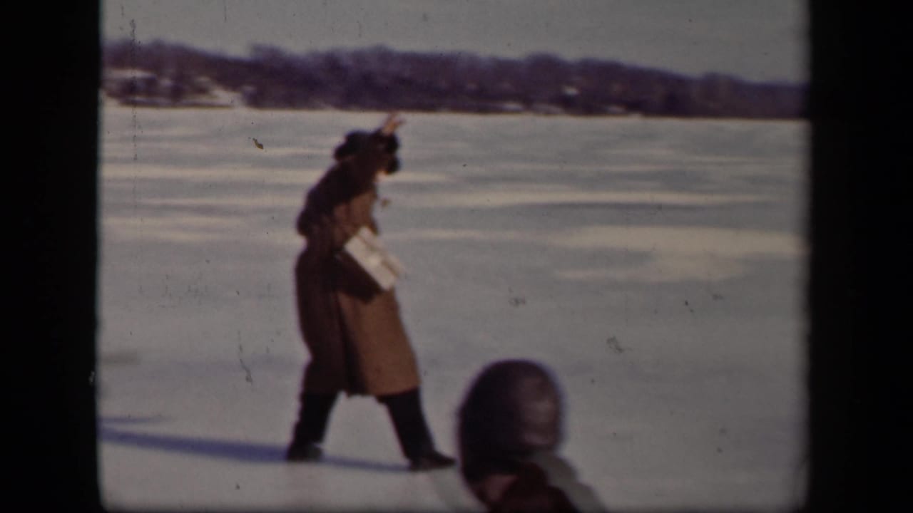 A man in a long coat appears to regain balance on the frozen lake in Sebring, Ohio, while a bundled foreground figure enters the frame.