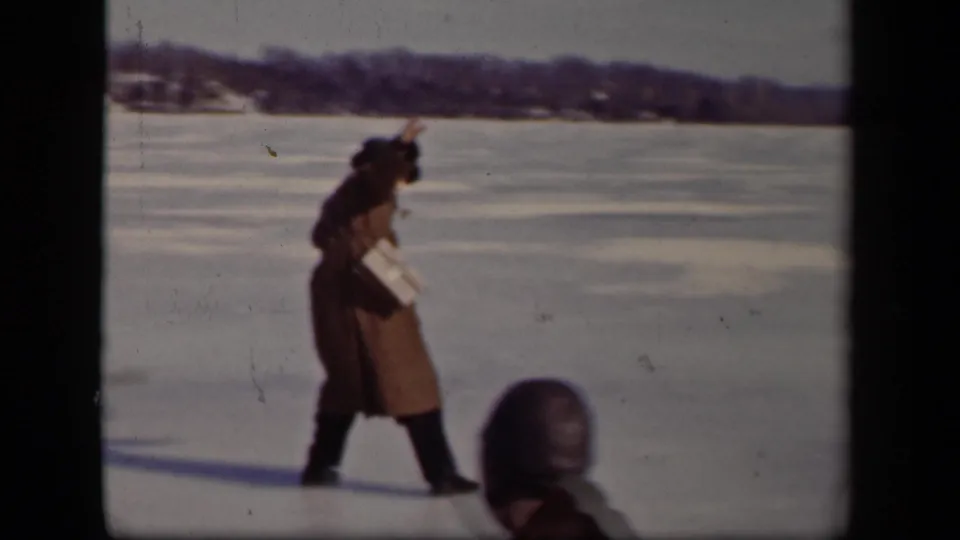 A man in a long coat appears to regain balance on the frozen lake in Sebring, Ohio, while a bundled foreground figure enters the frame.