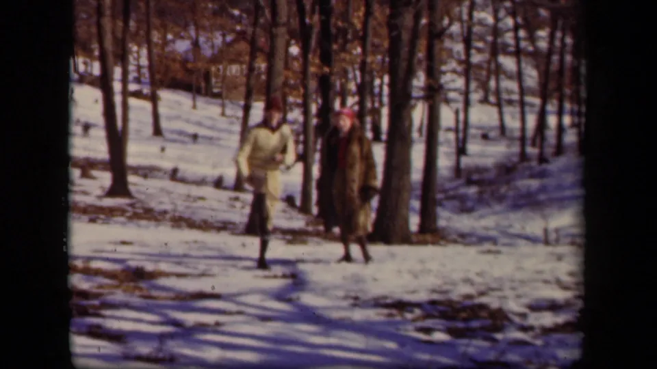 Two adults continue along a snowy wooded area, with a faint house visible beyond the trees in the Sebring, Ohio footage.
