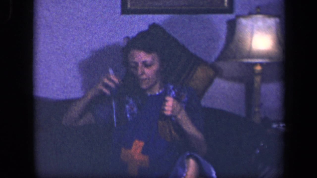In a 1942 Sebring, Ohio home-movie frame, a woman sits on a couch with knitting materials near a warm table lamp.