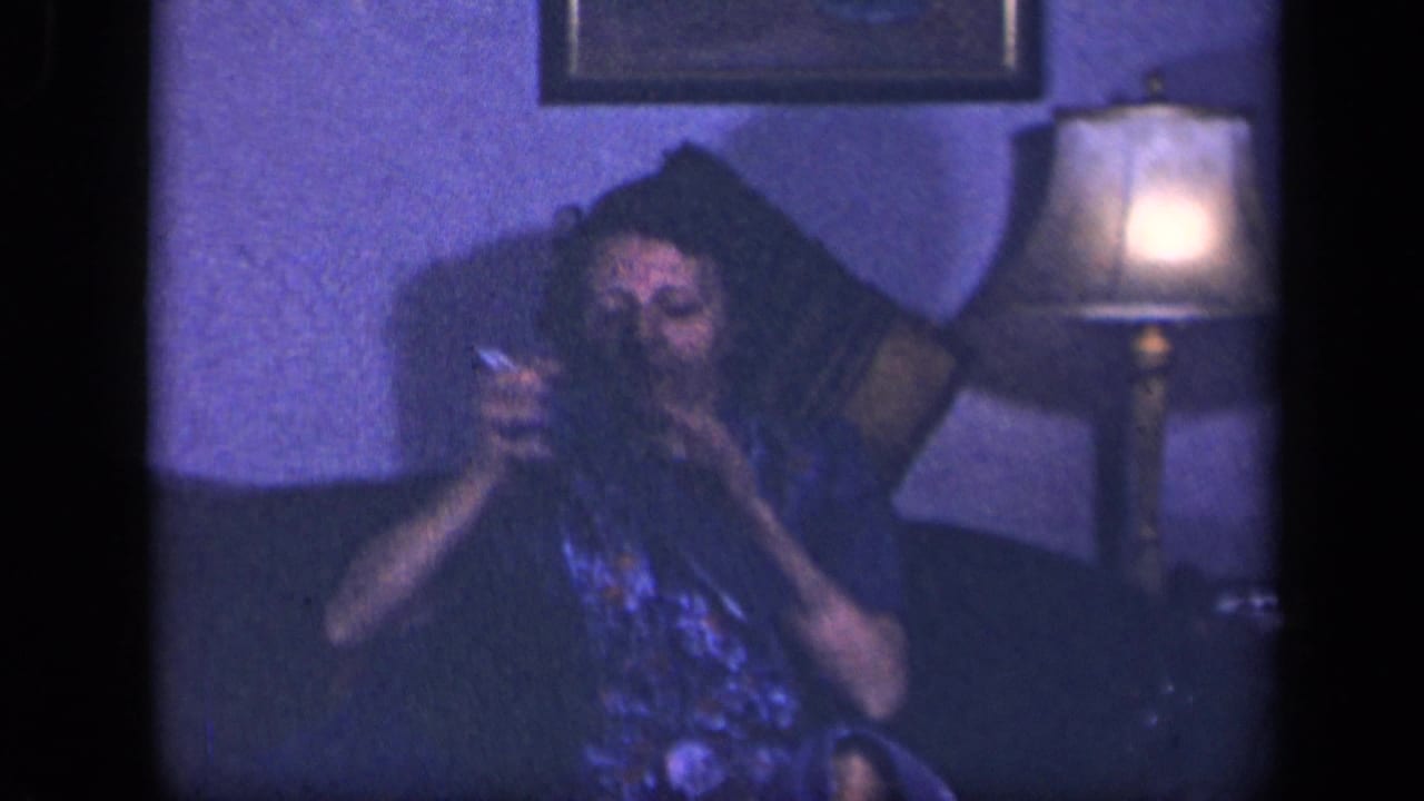 The woman appears to inspect or work on her knitting while seated in a Sebring, Ohio living room, with a lamp glowing beside her.