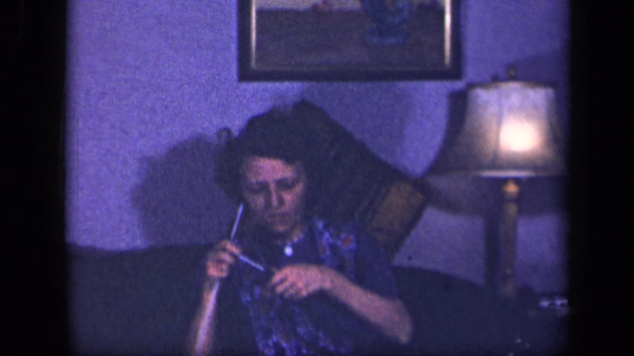 Woman seated on a couch knitting beside a lit table lamp.