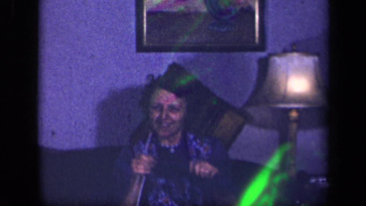 Smiling woman holds knitting needles on a couch near a lamp.