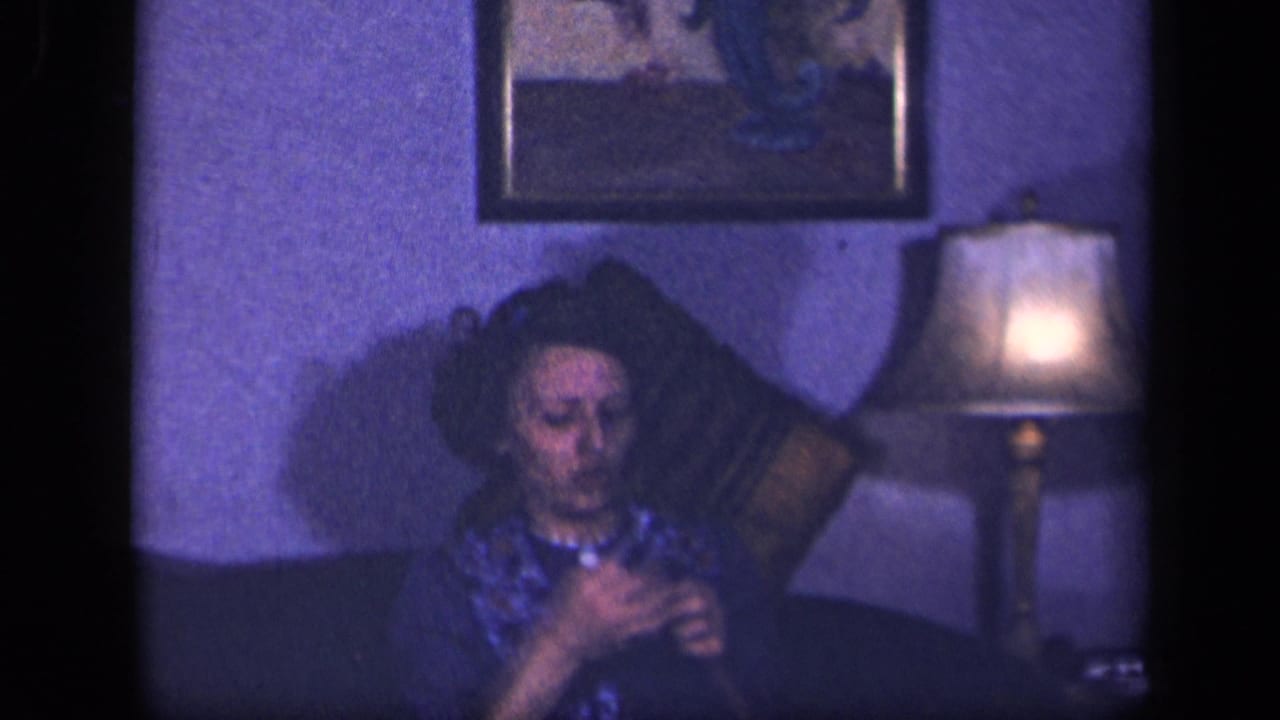 Woman seated on a couch crocheting beside a lit table lamp.