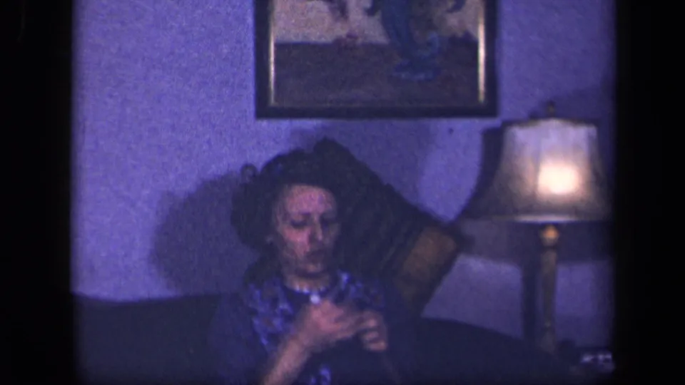 In Sebring, Ohio home-movie footage from 1942, a woman sits on a couch crocheting near a lit lamp and framed wall art.