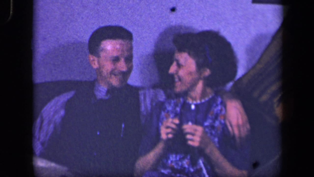 Adult couple sits close on a couch, smiling toward each other.