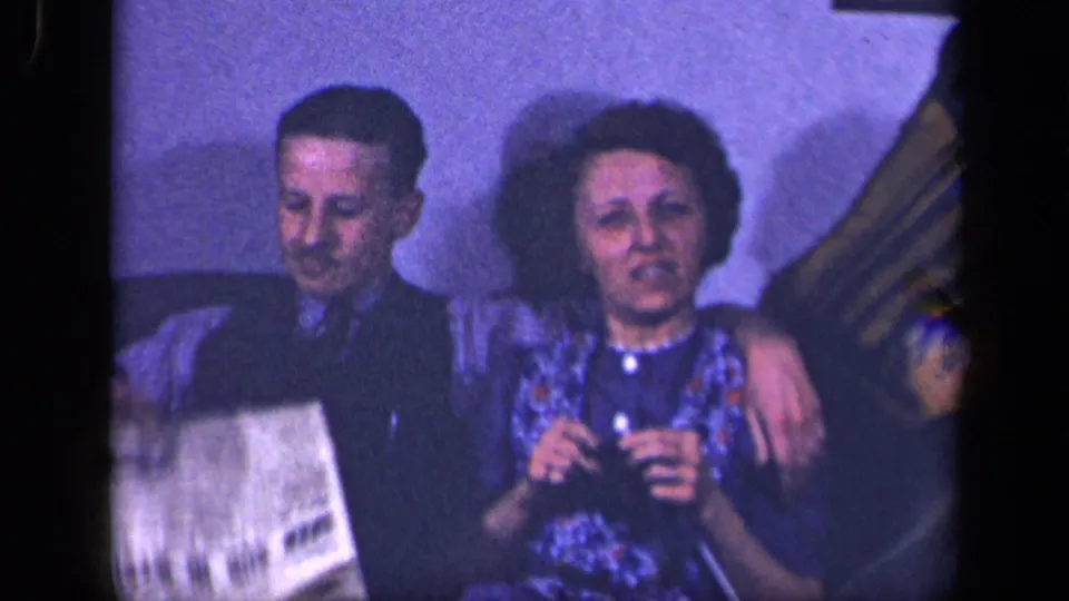 In the final frame, the woman faces forward with a small object in hand as the man sits beside her and a paper enters the foreground.