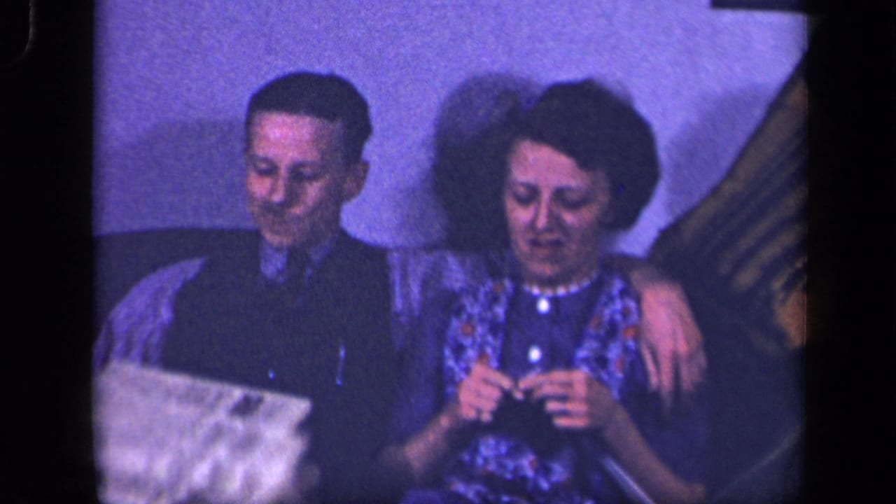 In a 1942 Sebring, Ohio home-movie frame, a man in a dark vest sits beside a woman knitting on a sofa.
