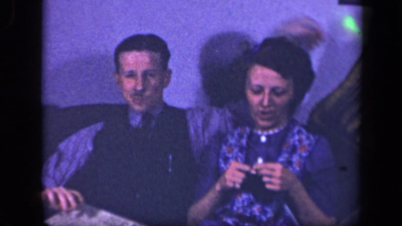 Man and woman sit together as she knits and an arm moves behind her.
