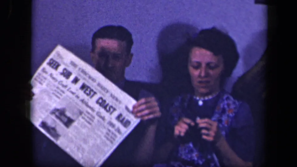 The man lifts a newspaper on the sofa while the woman keeps knitting in the 1942 Sebring, Ohio home-movie scene.