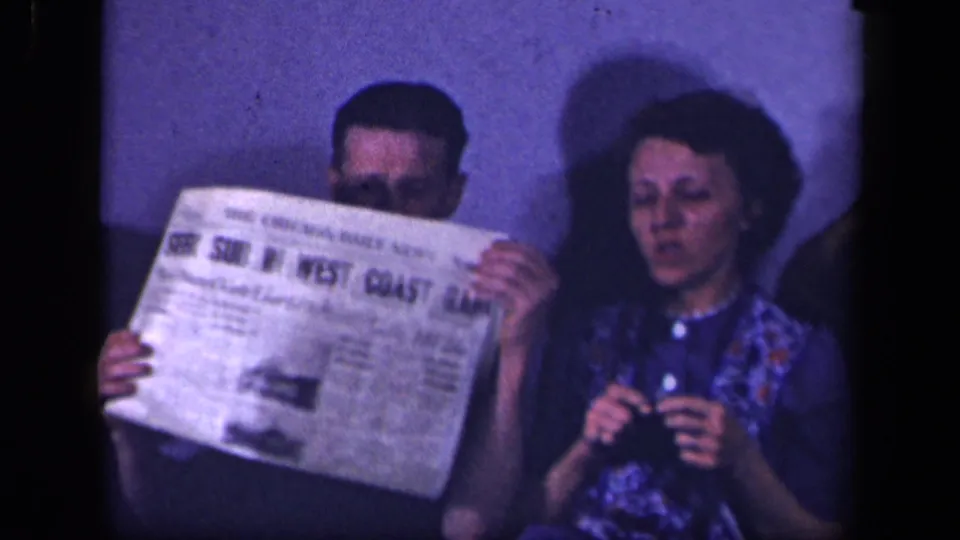 The man reads or holds up a newspaper next to the knitting woman in the Sebring, Ohio domestic interior.