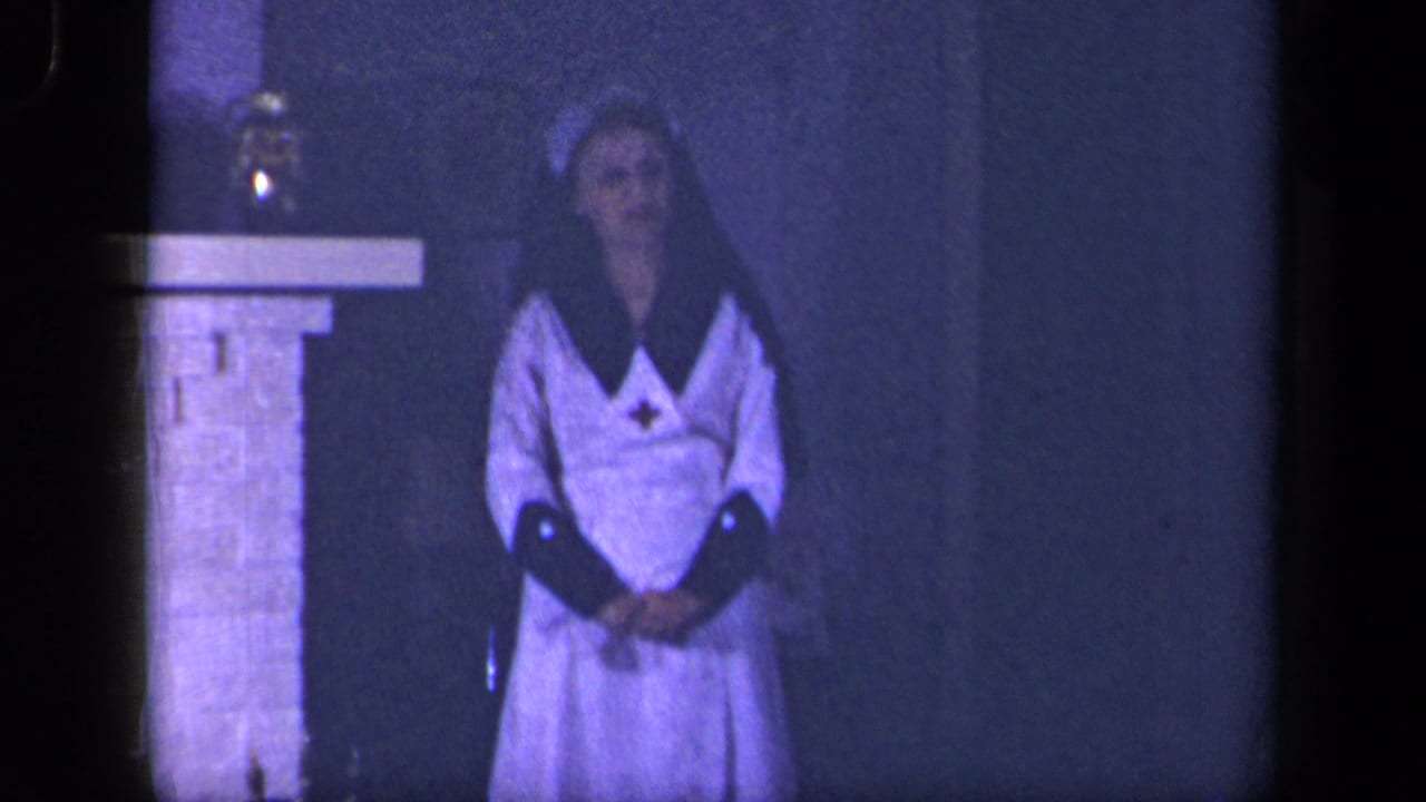 The woman stands with hands clasped in a white nurse-style dress and cap beside a fireplace in the 1942 Sebring, Ohio interior scene.