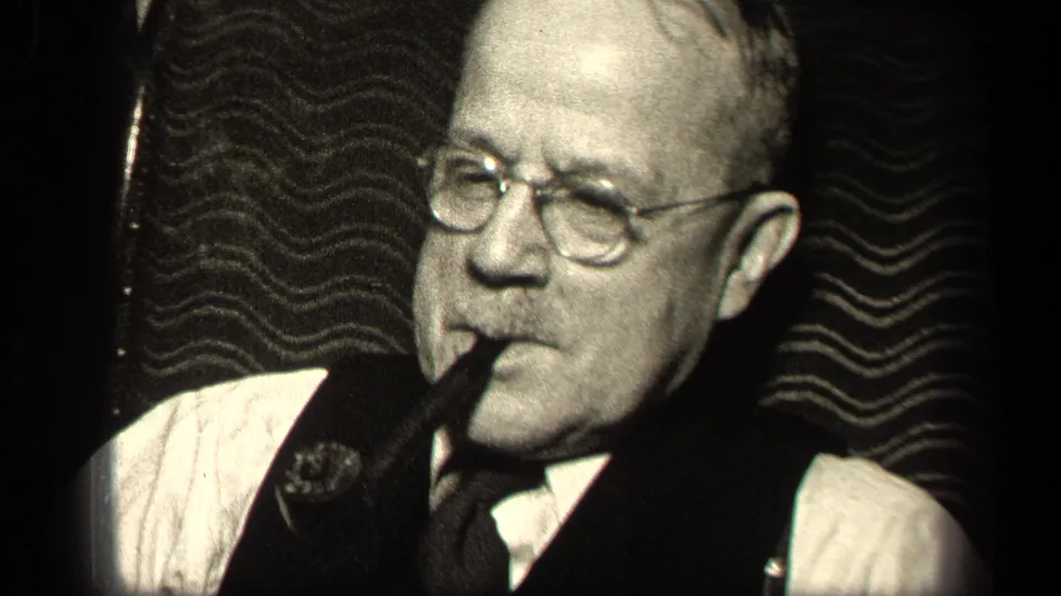 1942 Sebring, Ohio home-movie frame showing an older man in glasses, vest, white shirt, and tie smoking a pipe.
