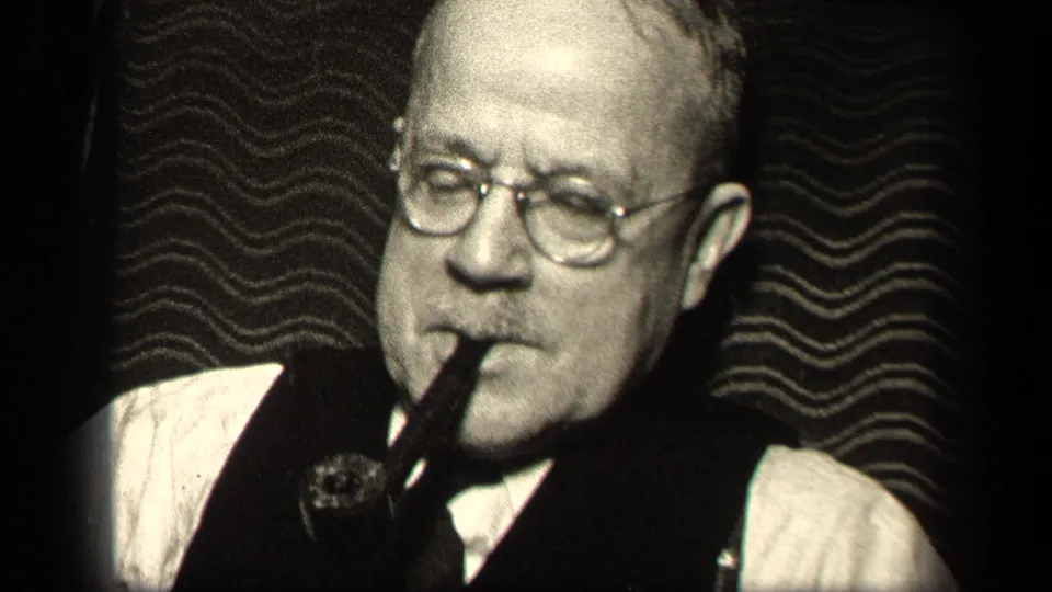 1942 Sebring, Ohio frame of an older man wearing glasses and a vest, pipe held at his mouth in close-up.