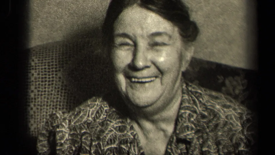 Older woman in a patterned blouse smiles toward the camera in black-and-white 8mm home-movie footage tied to Sebring, Ohio, 1942 metadata.