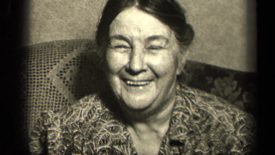 Older woman laughs in a close indoor portrait, with patterned blouse and chair fabric visible in 1942 Sebring, Ohio home-movie metadata.