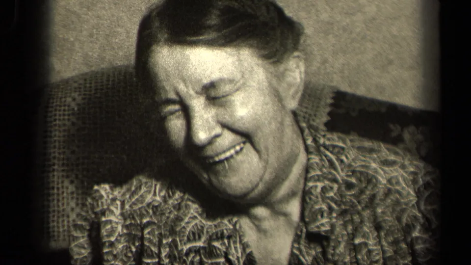 In a 1942 Sebring, Ohio 8mm home movie frame, an older woman laughs while seated in a patterned armchair indoors.