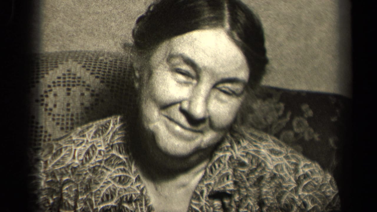 1942 Sebring, Ohio frame of a seated elderly woman smiling gently, with patterned clothing and a textured chair back visible.