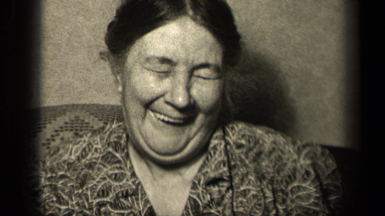 Woman laughing in a patterned blouse while seated indoors.
