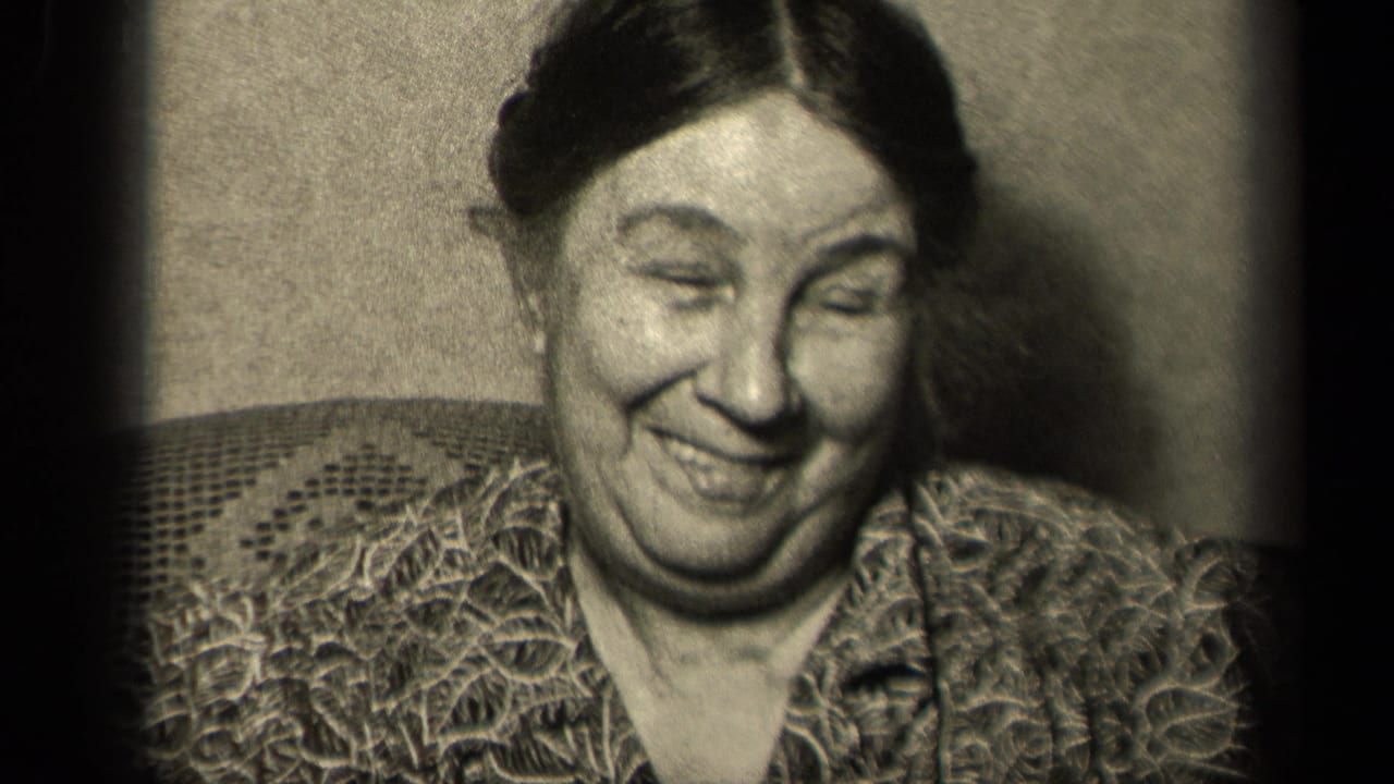 In 1942 Sebring, Ohio home-movie footage, a woman smiles downward in a patterned blouse beside an upholstered chair back.