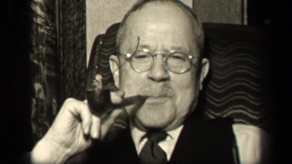 In 1942 Sebring, Ohio footage, an older man in glasses and formal clothing holds a pipe while seated in a wavy-patterned chair.
